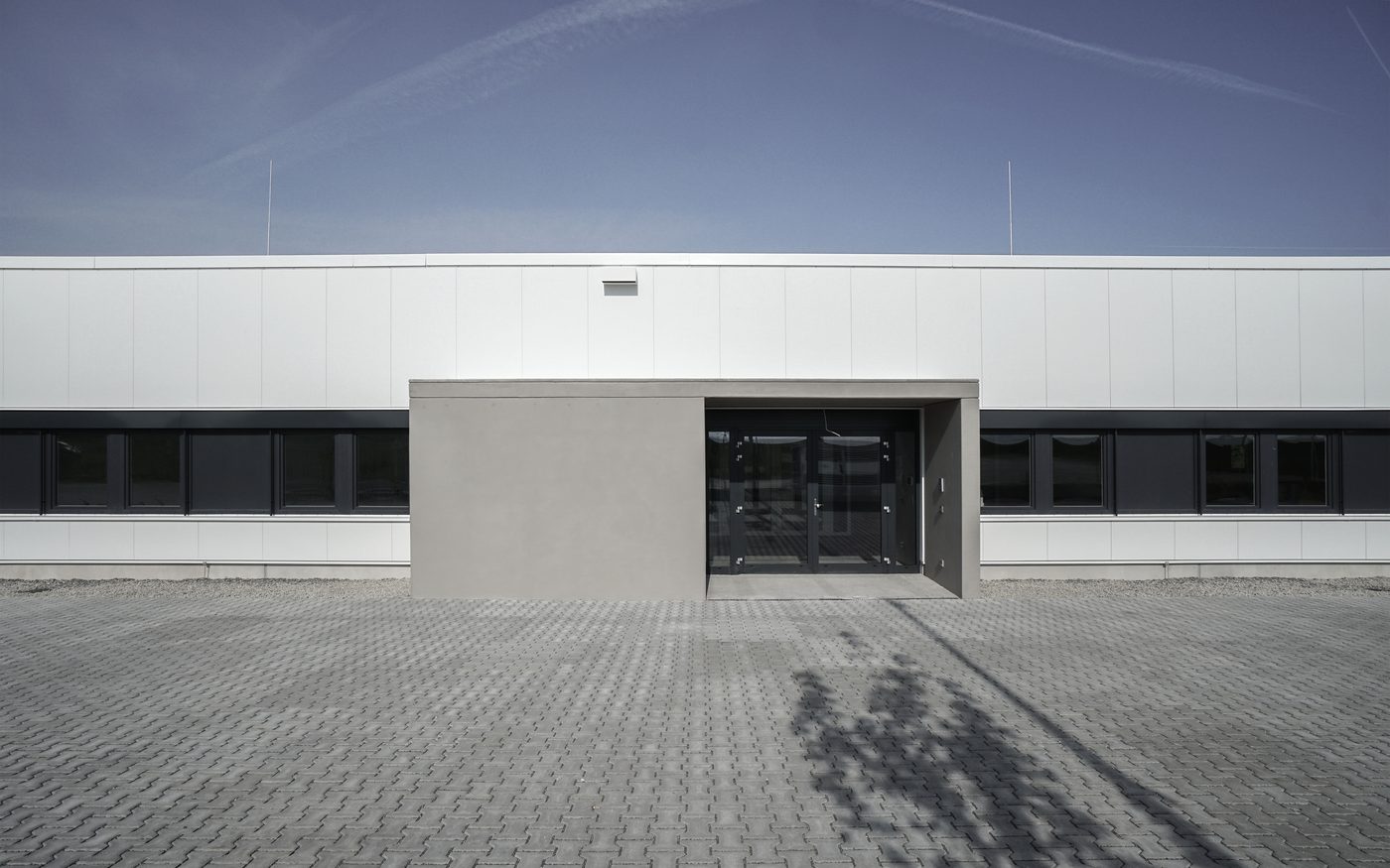 Weiße Produktionshalle mit Eingangsbaukörper aus Sichtbeton