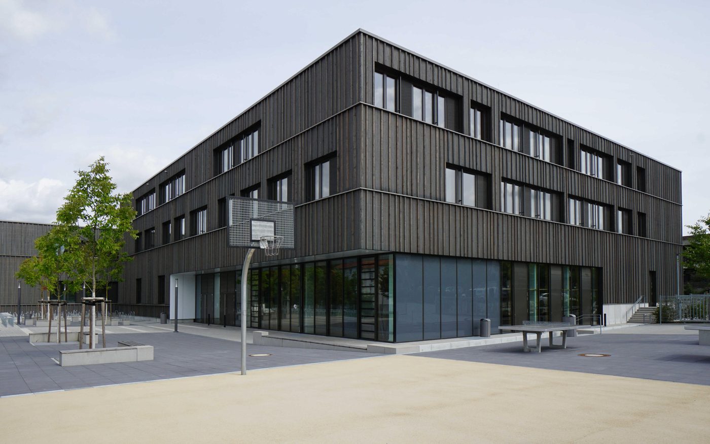 Neubau der Gymnasialen Oberstufe Frankfurt mit dunkler Holzfassade und Schulhof